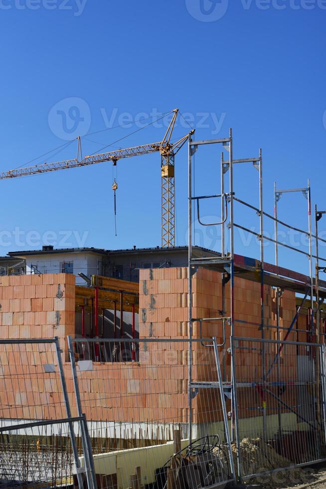 Close up of the shell of a stone house on a construction site for a residential area, with a blue sky and crane in the background photo