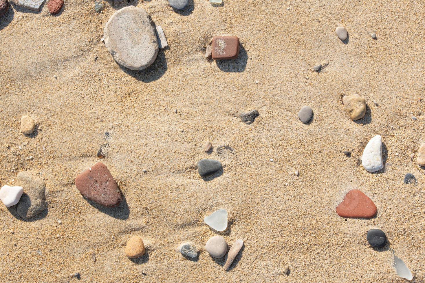 Background and texture of the sandy beach on which stones, carved by the sea, lie on the sun shines photo