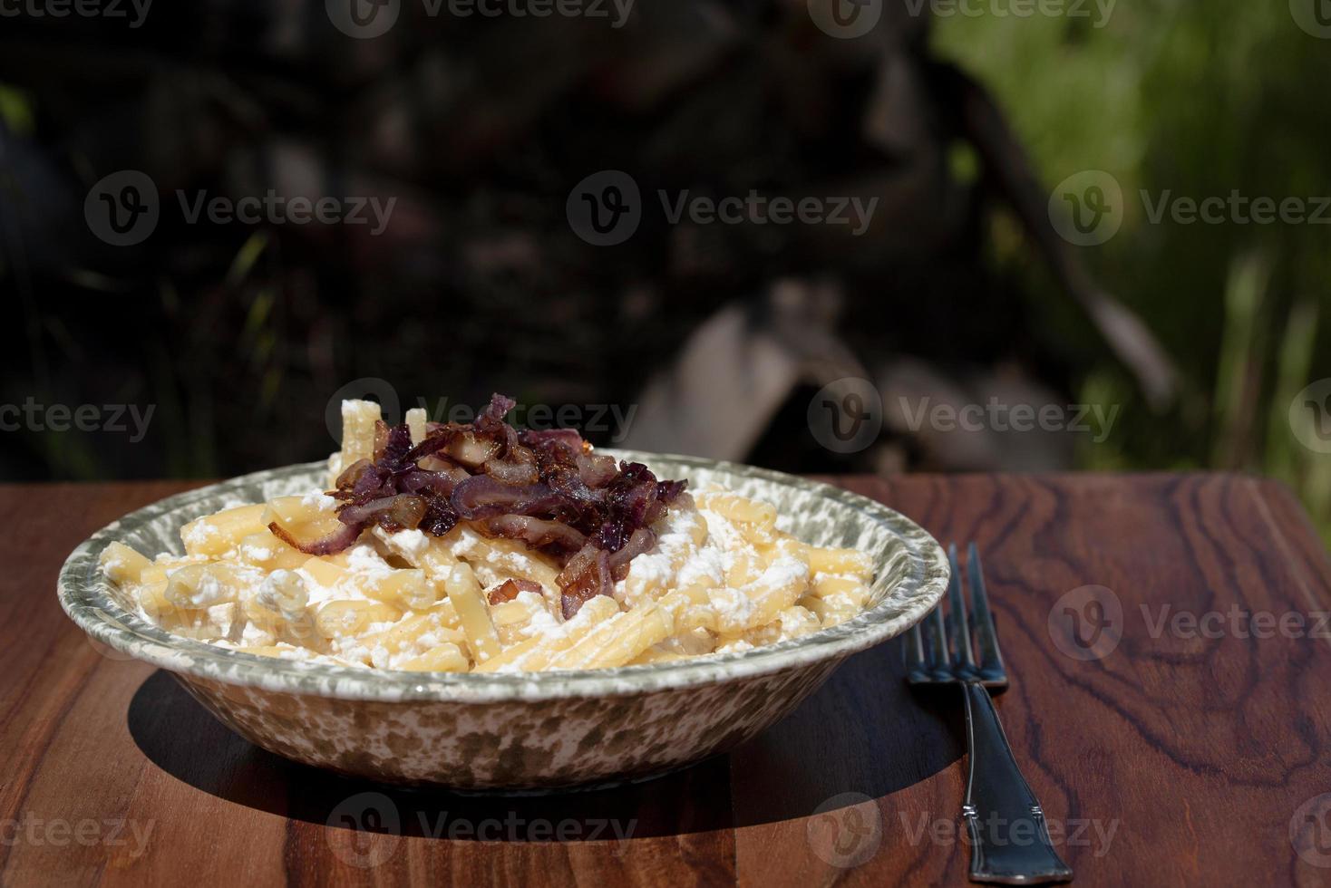 A plate of pasta and ricotta, as well as roasted onions, is on a wooden table, with a fork next to it, ready to eat photo