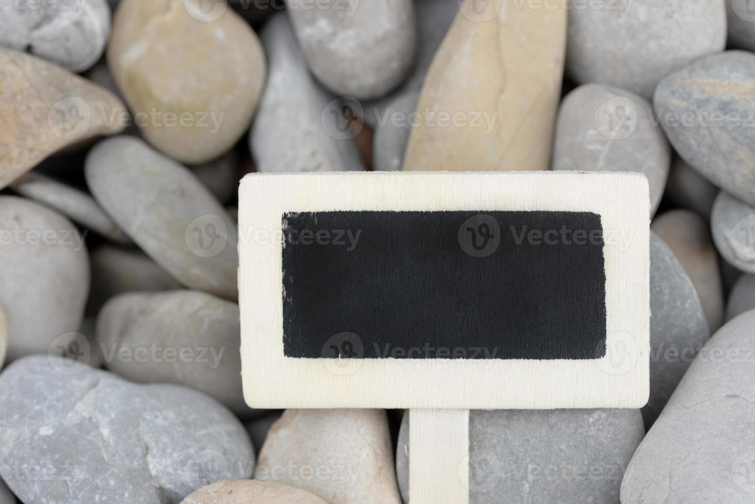 A small wooden sign with a black writing surface in front of gray pebbles as a background photo