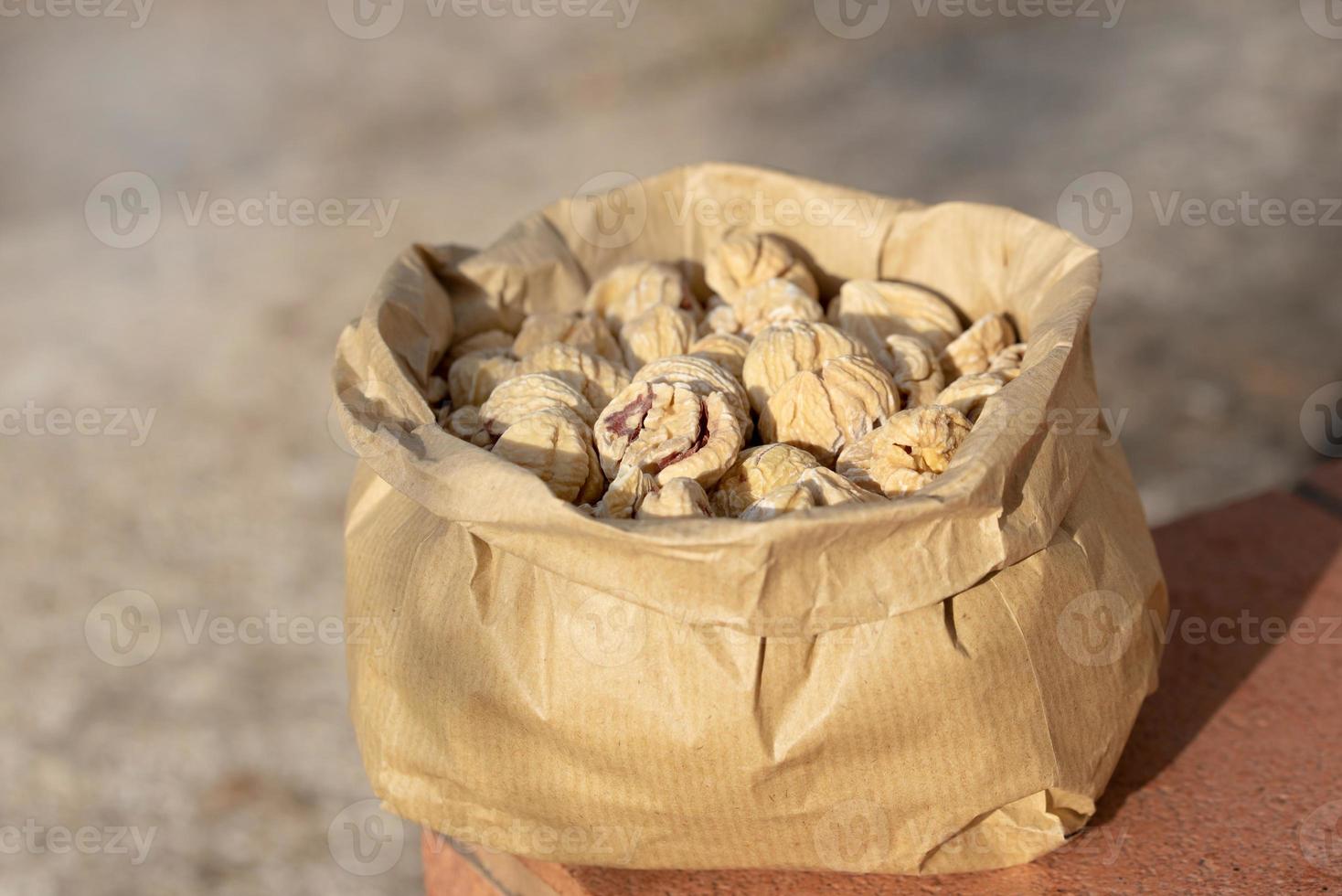 There are a lot of dried chestnuts in a paper bag that is in the open air photo