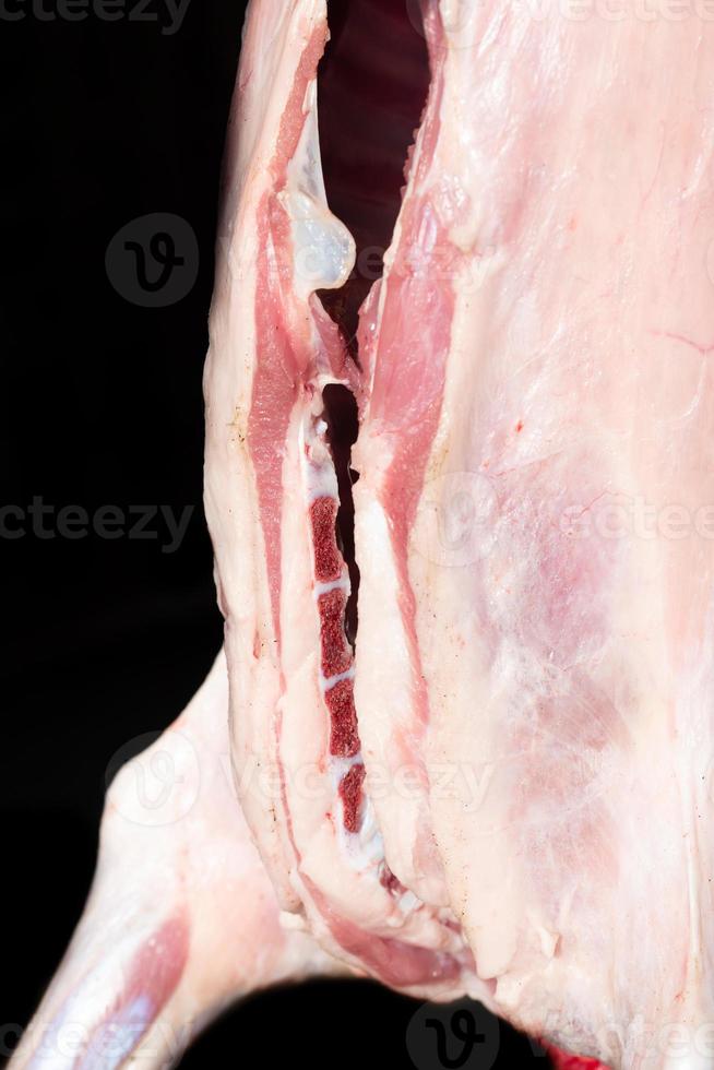 Detail of a lamb slaughtered in the traditional way, skinned and hanging in front of a dark background. The animal was divided along the spine photo