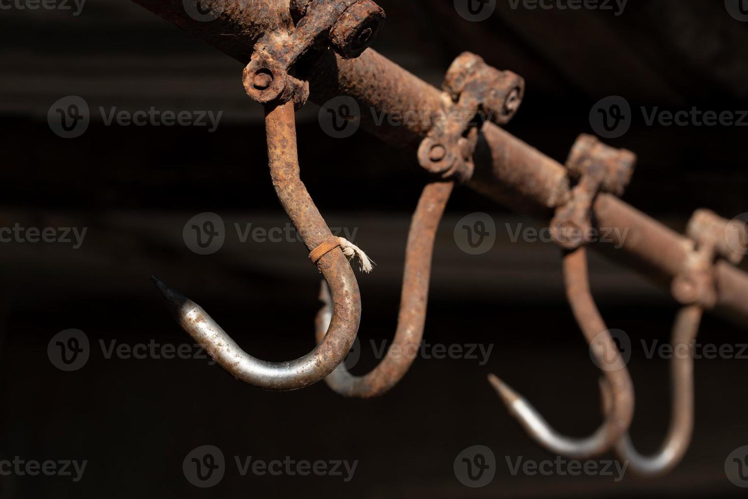 Rusty meat hooks hang from the ceiling against a dark background photo