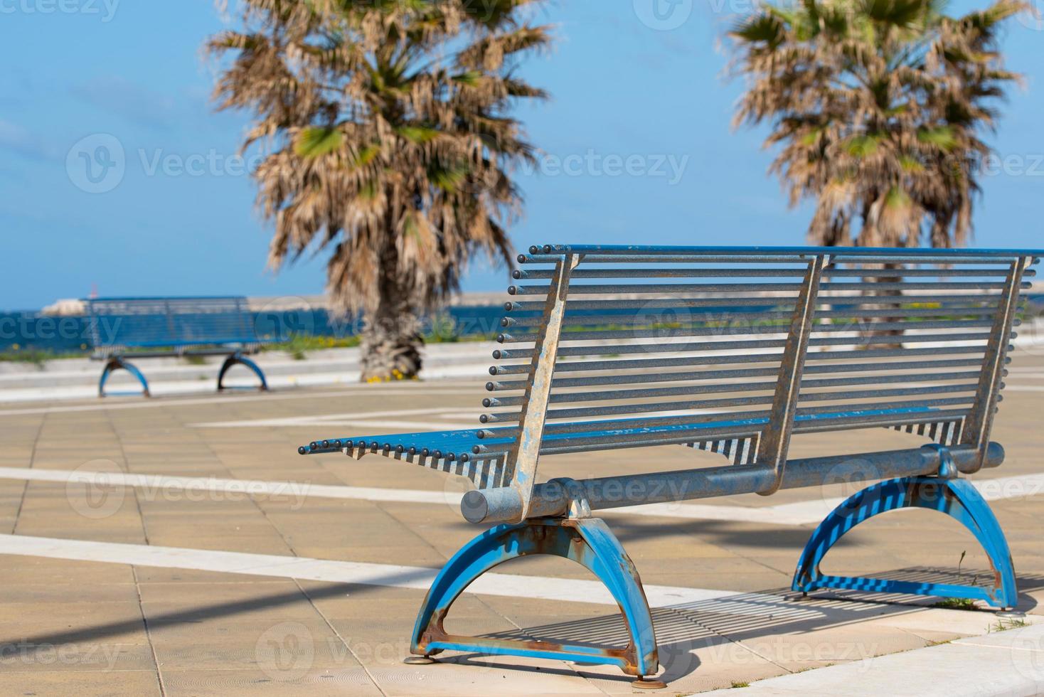 In Italy on the beach promenade there are empty metal benches and palm trees in the background. The promenade is deserted photo