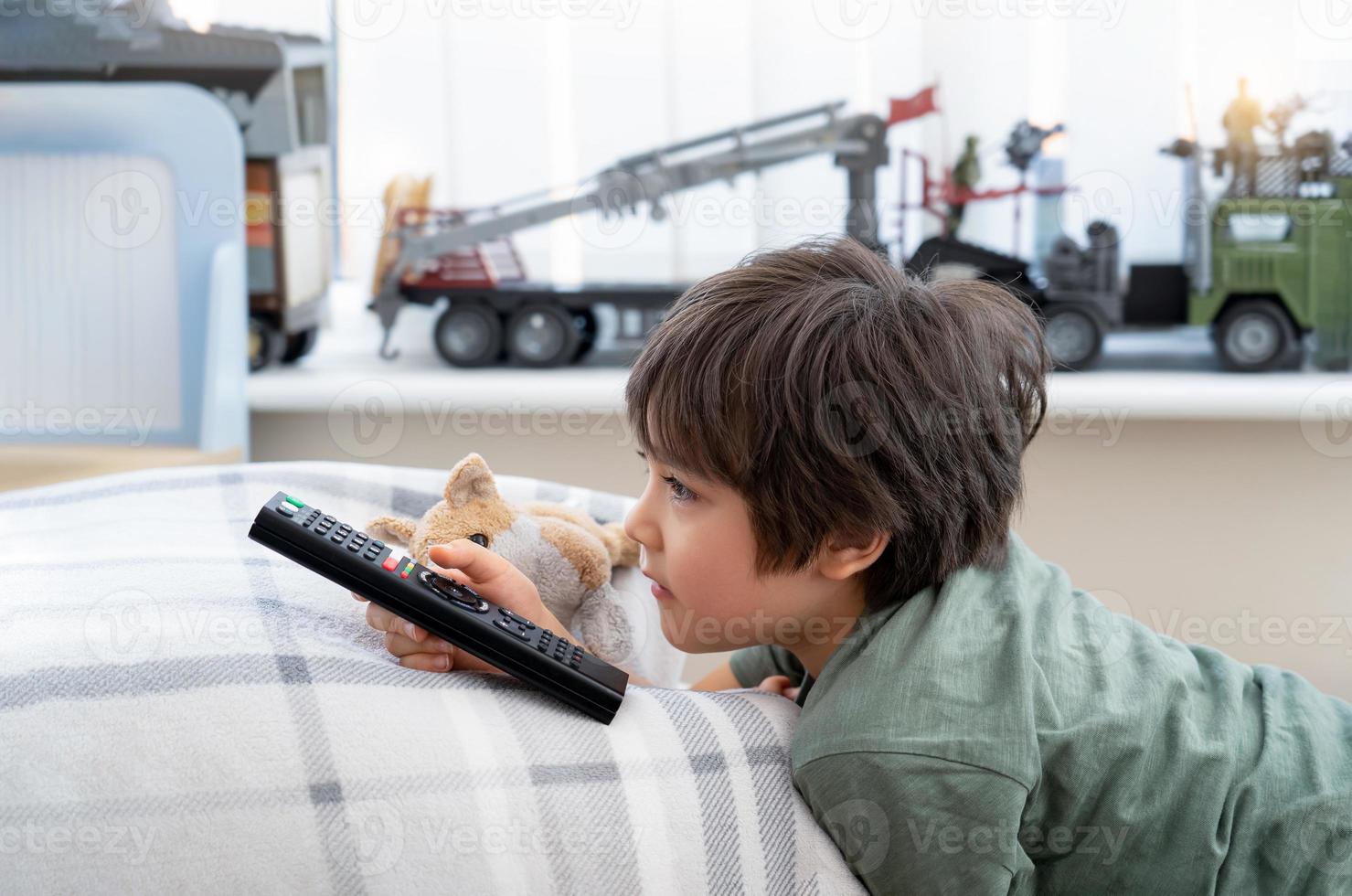 Portrait of happy kid lying on sofa watching TV, Positive child boy holding remote control looking out with smilng face.Healthy child stay at home during covid-19 lock down, Social Distance photo