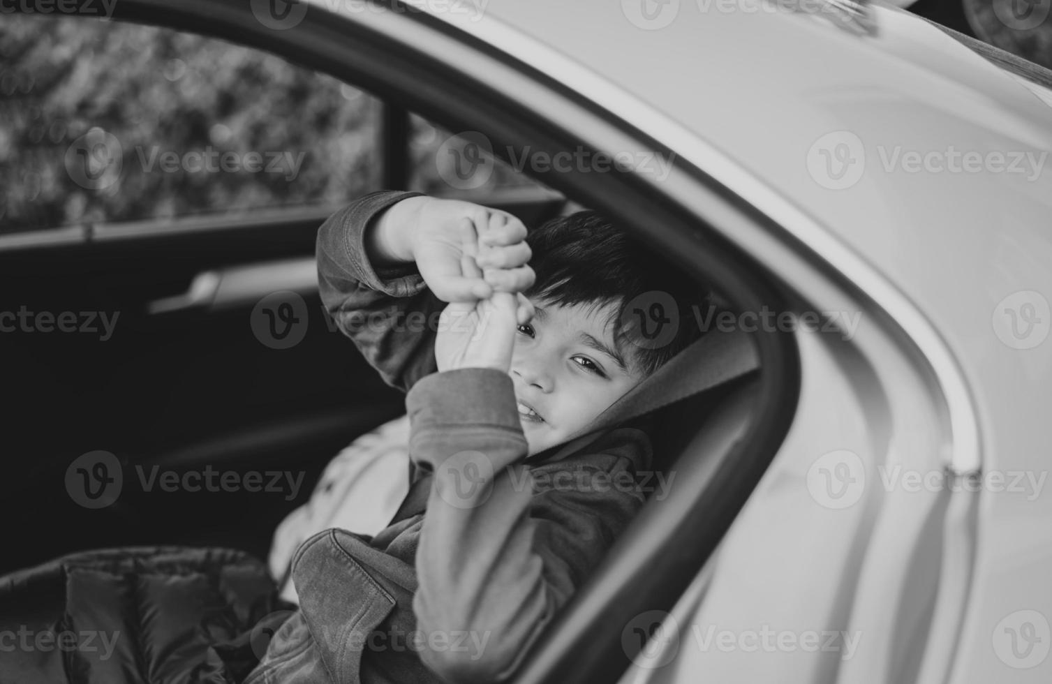 Black and White Portrait Happy boy siting in safety car seat looking at camera with smiling face,Child sitting in the back passenger seat with a safety belt, School kid traveling to school by car photo