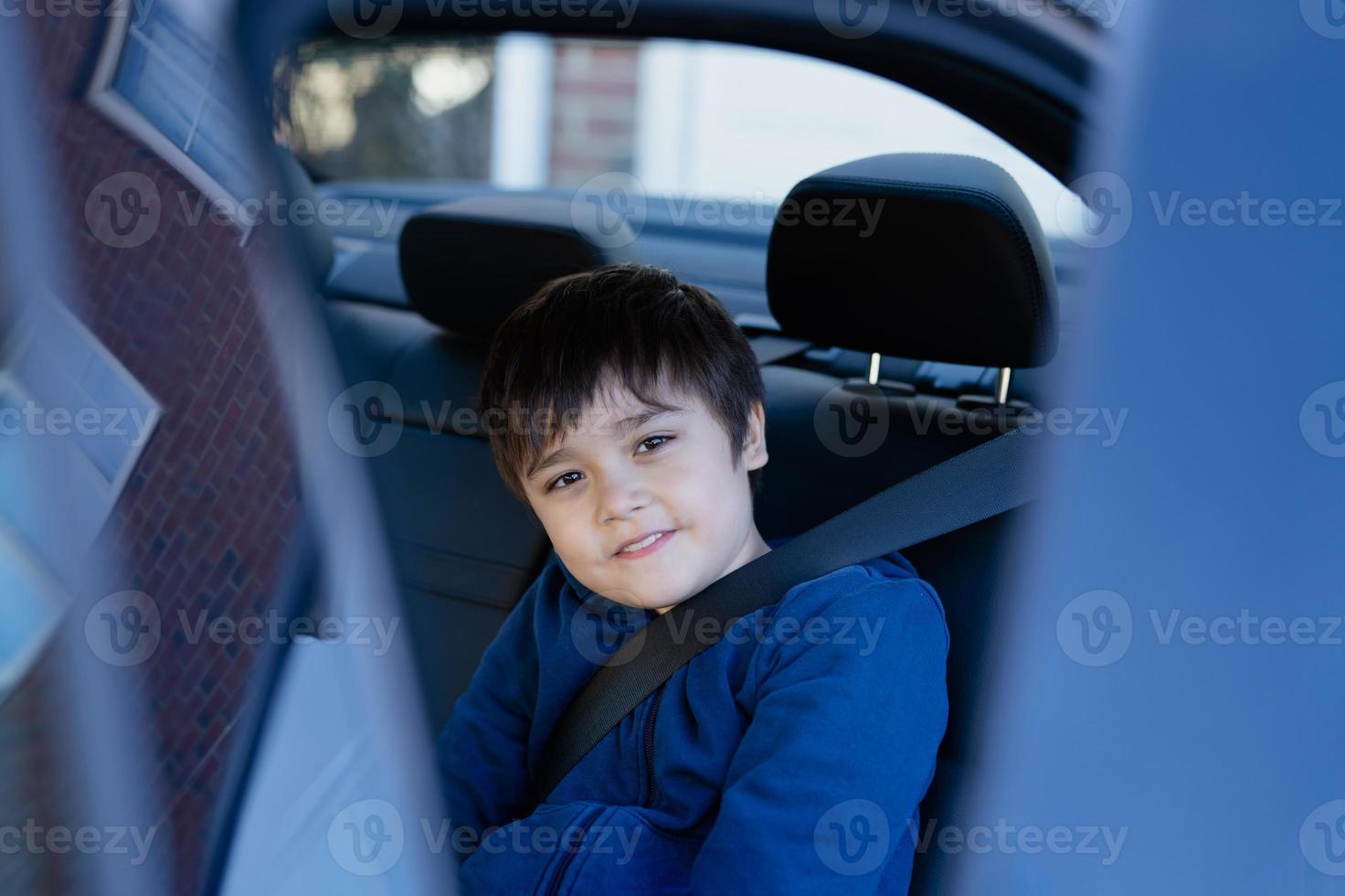 Cinematic portrait boy siting in safety car seat looking at camera with smiling face,Child sitting in the back passenger seat with a safety belt, School kid traveling to school by car.Back to school photo