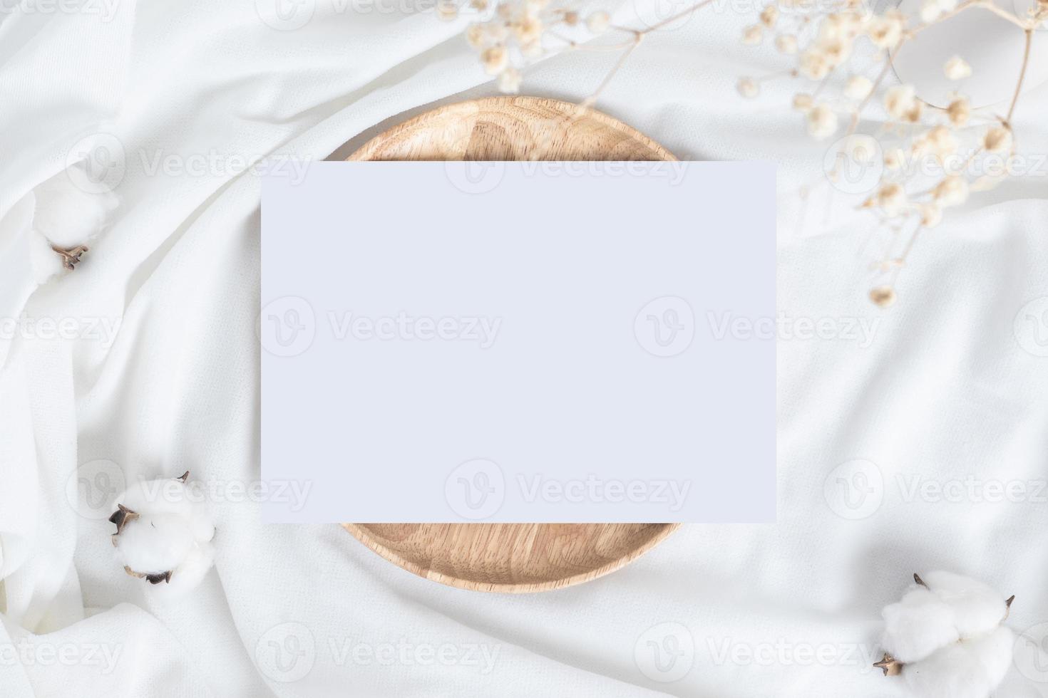 una mesa con flores de algodón y un plato o bandeja de madera y una tarjeta en blanco. foto