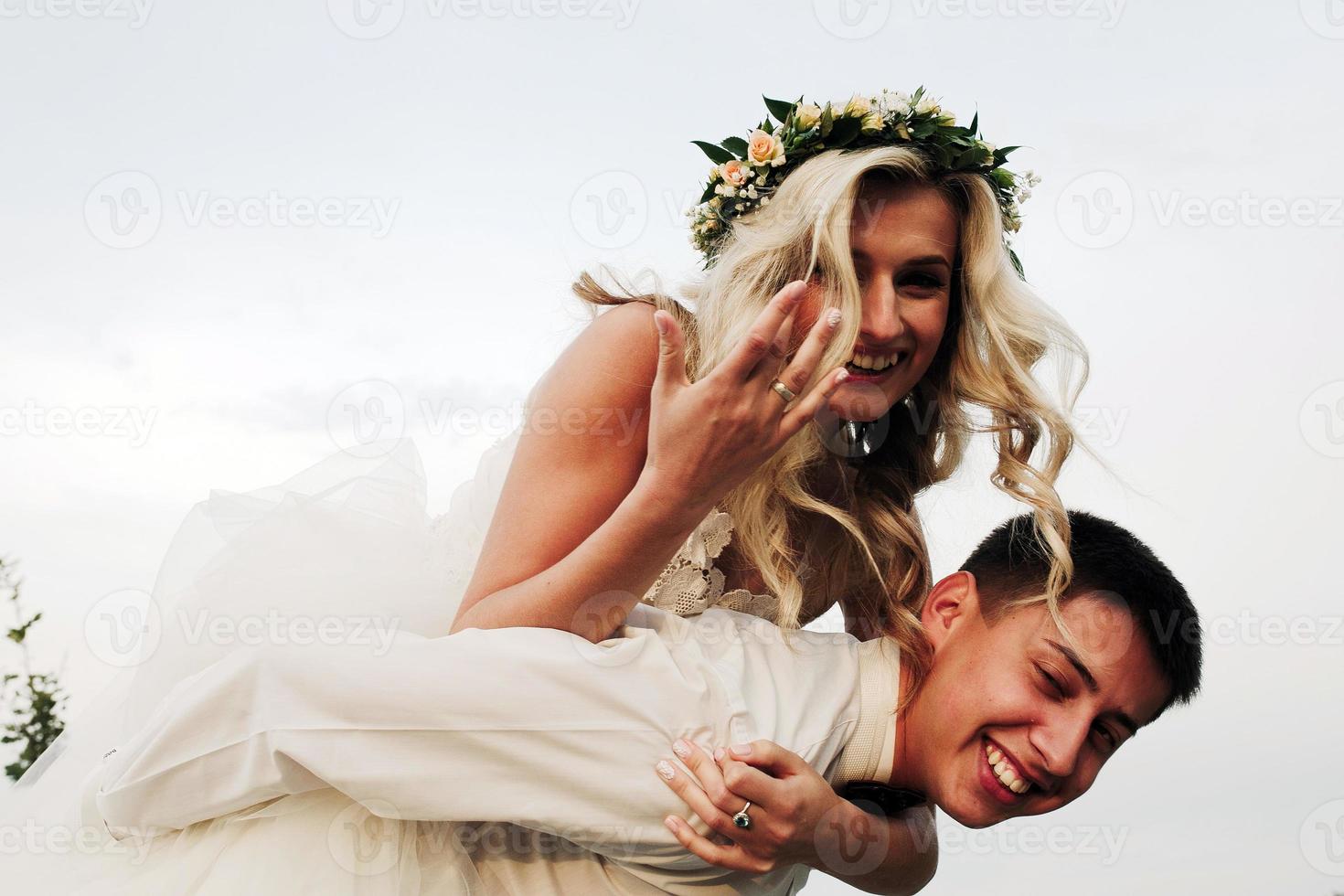 groom carries bride on his back outdoors photo