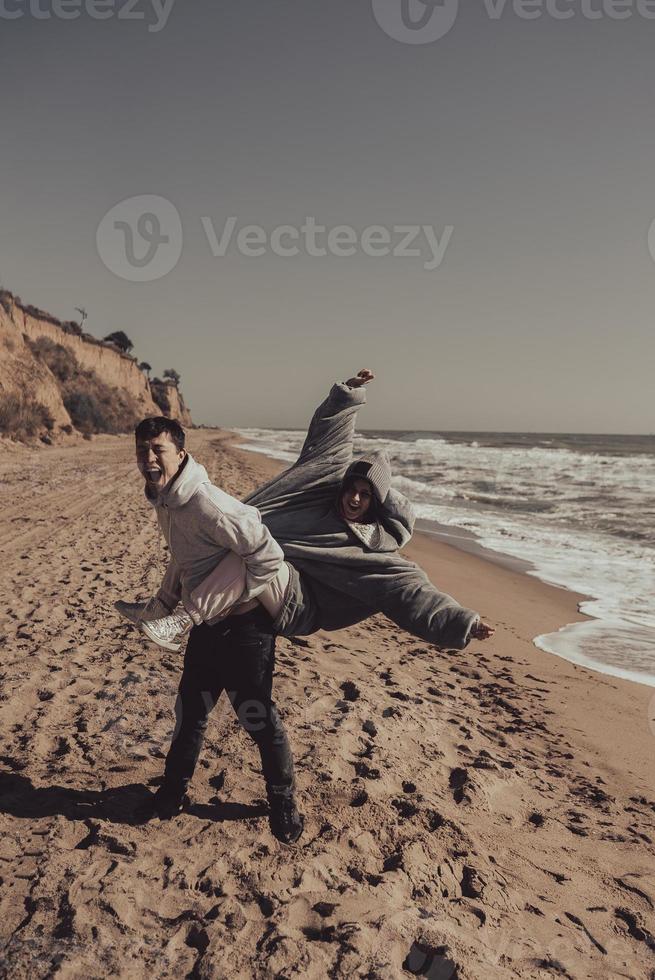 Man carries his girlfriend on back, couple having fun on the seashore photo