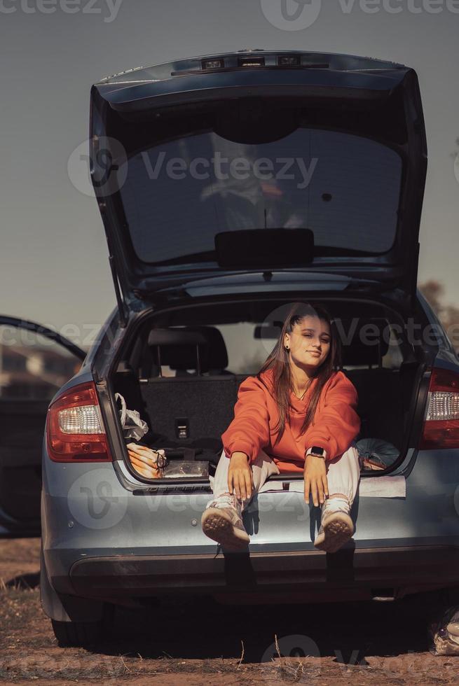 joven atractiva descansando en el maletero de un coche foto
