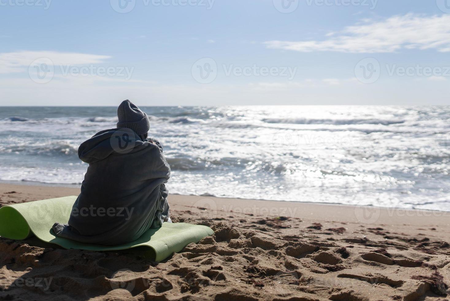 Pretty woman in warm clothes sitting on the cold autumn beach. photo