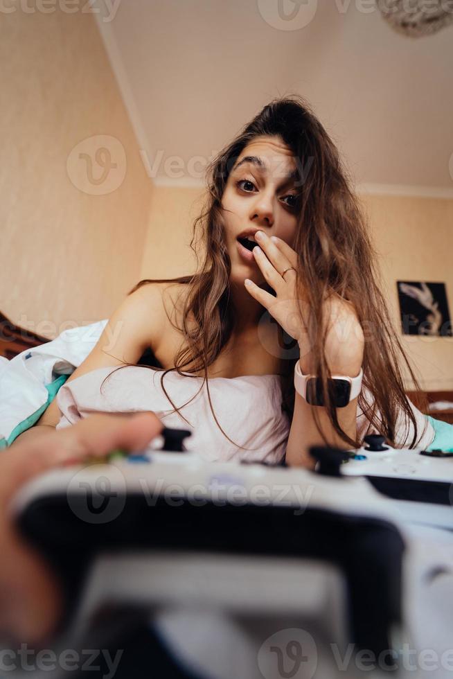 chica divertida acostada en la cama y jugando videojuegos, sosteniendo el controlador foto