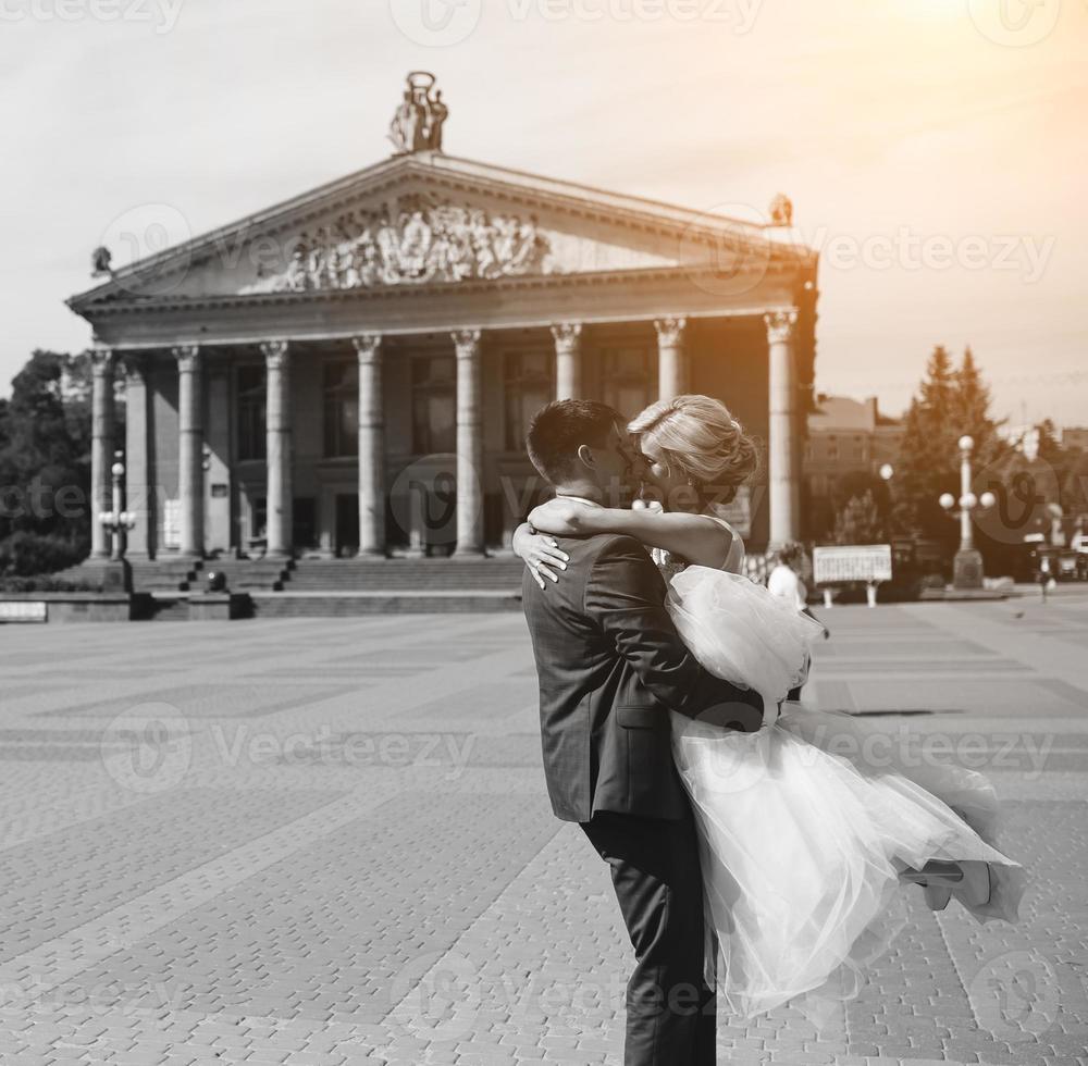 groom holds bride in his arms and twisted photo