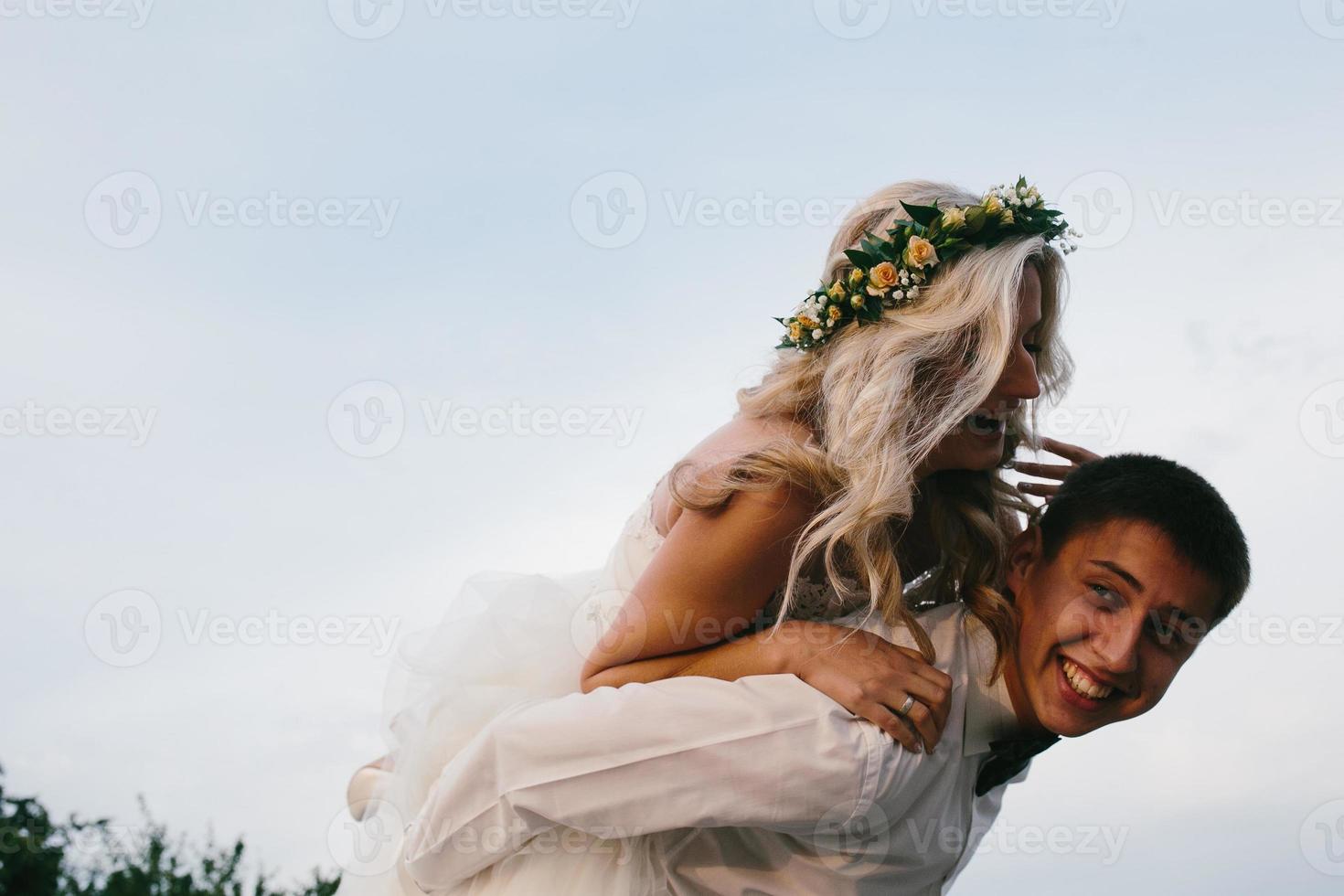 el novio lleva a la novia en la espalda al aire libre foto