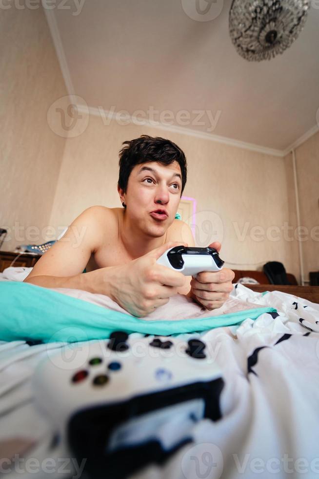 Guy lying in bed and playing video game, holding controller photo