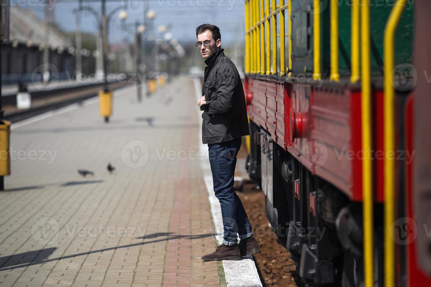 A man dressed in jeans on the background of the train and the station photo