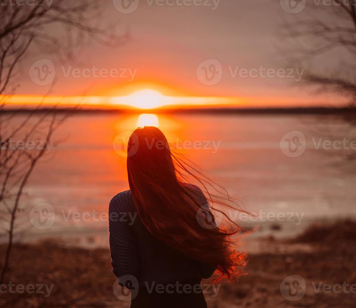 Woman enjoying time relaxing by the beautiful lake at sunrise. photo