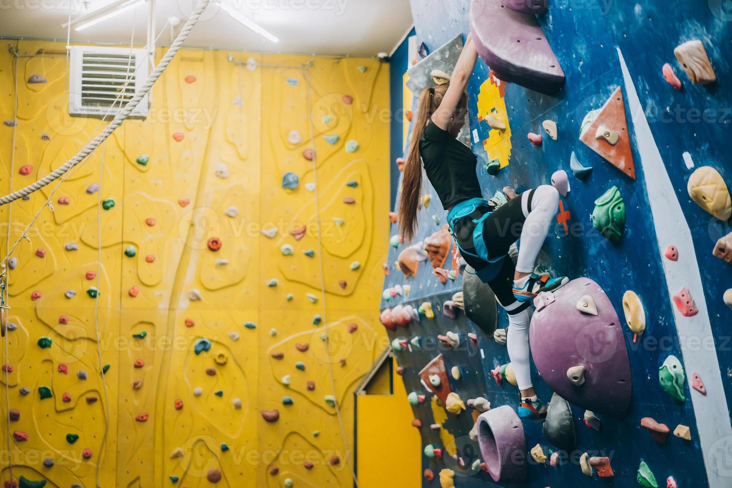 Young woman climbing a tall, indoor, man-made rock climbing wall photo