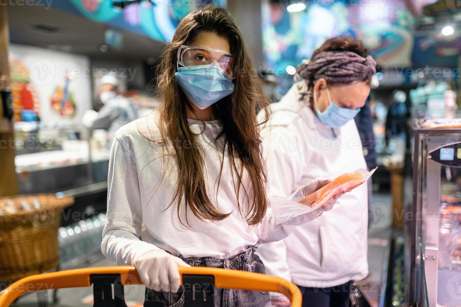 mujer con mascarilla quirúrgica y guantes está comprando en el supermercado foto