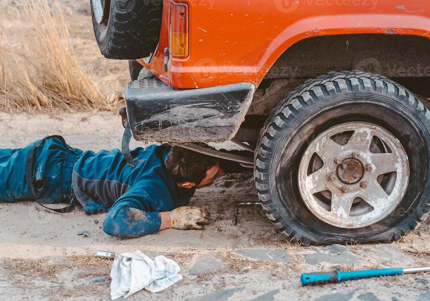 man lies under a 4x4 car on a dirt road photo