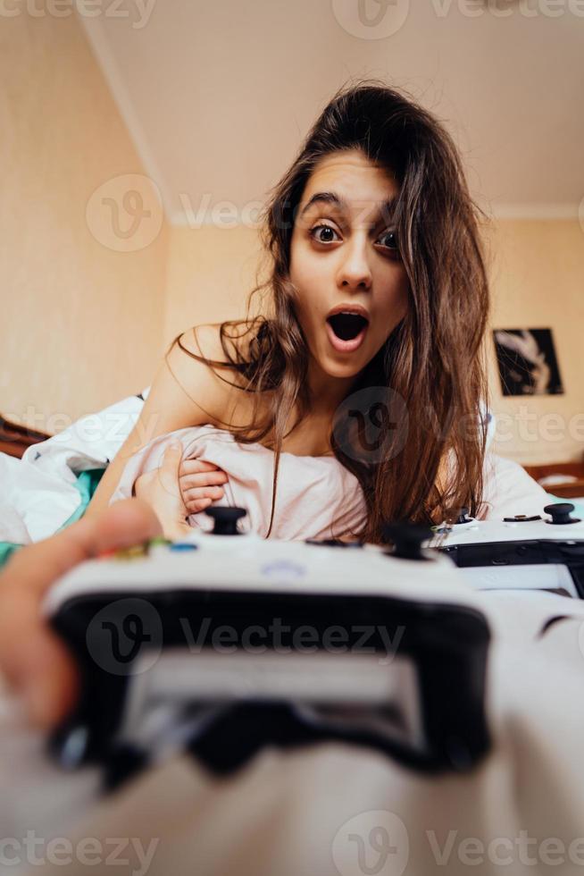 chica divertida acostada en la cama y jugando videojuegos, sosteniendo el controlador foto