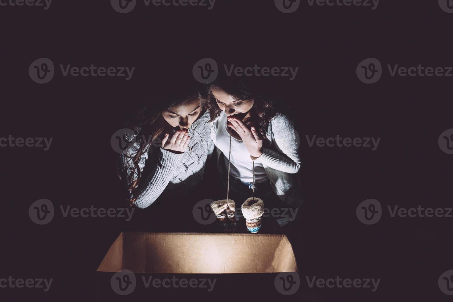 Sisters opens a box with a Christmas present and fascinated looks inside photo