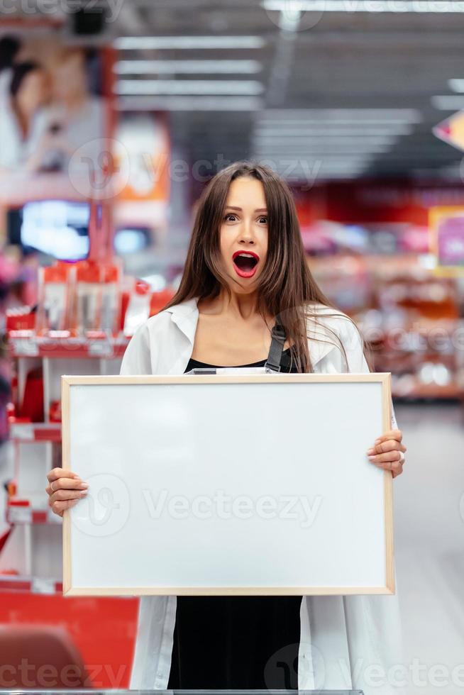 Smiling brunette woman holding white blank board photo