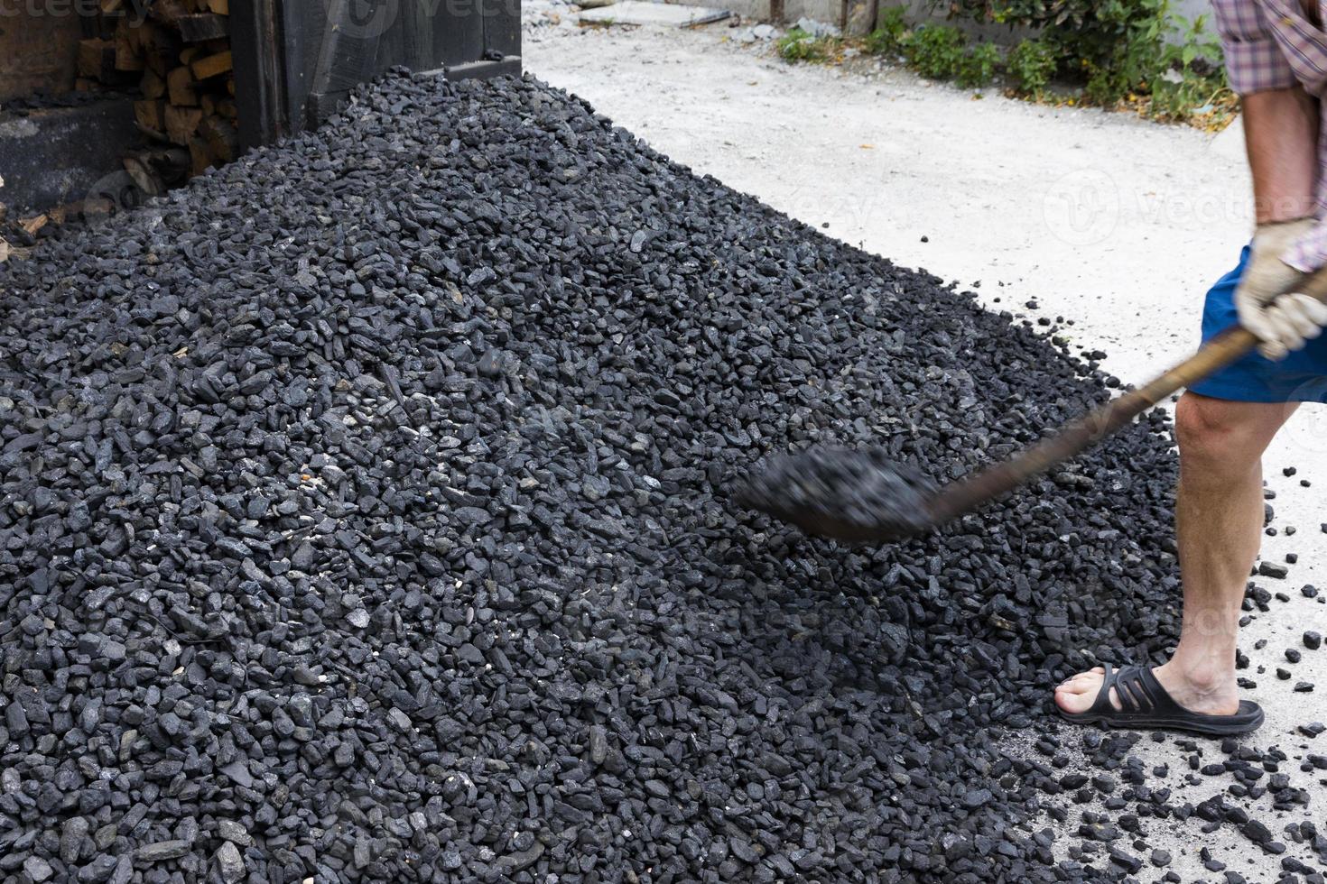 A worker with a shovel unloads black coal against the background of a large pile of coal. Soft focus. photo