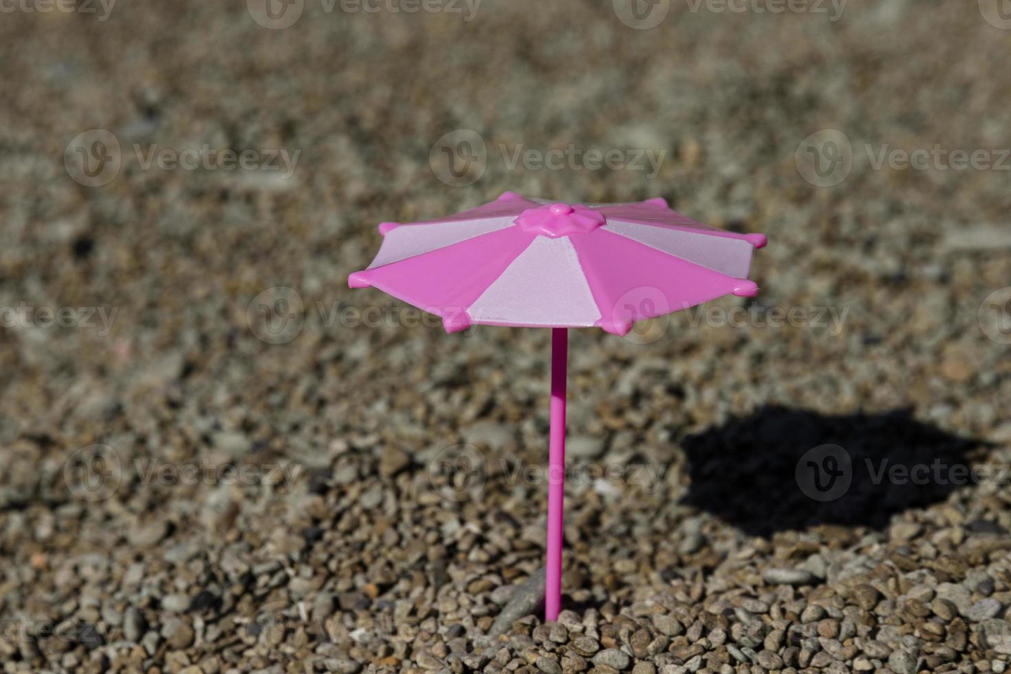 Toy umbrella with a shadow from the sun on a rocky beach, seashore. The concept of a place under the sun. photo