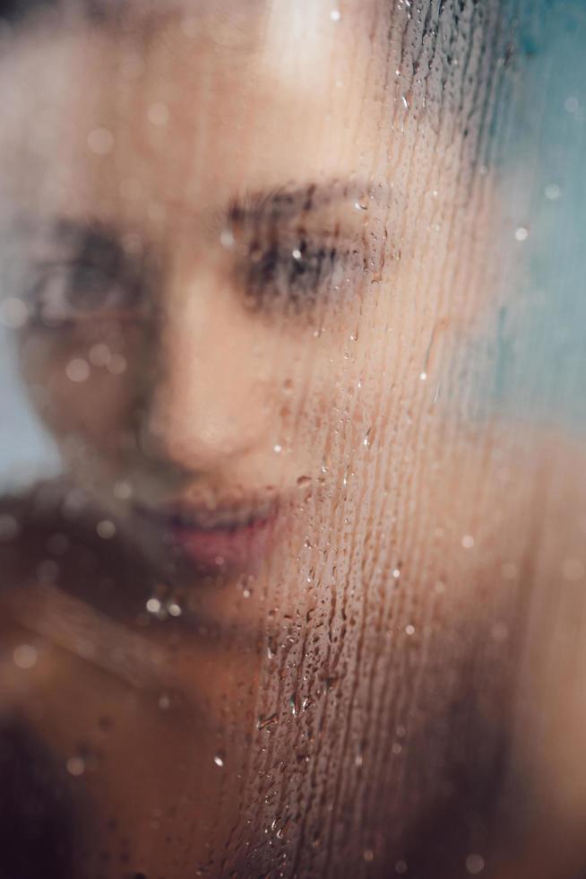 Beautiful woman behind the glass with water drops. photo