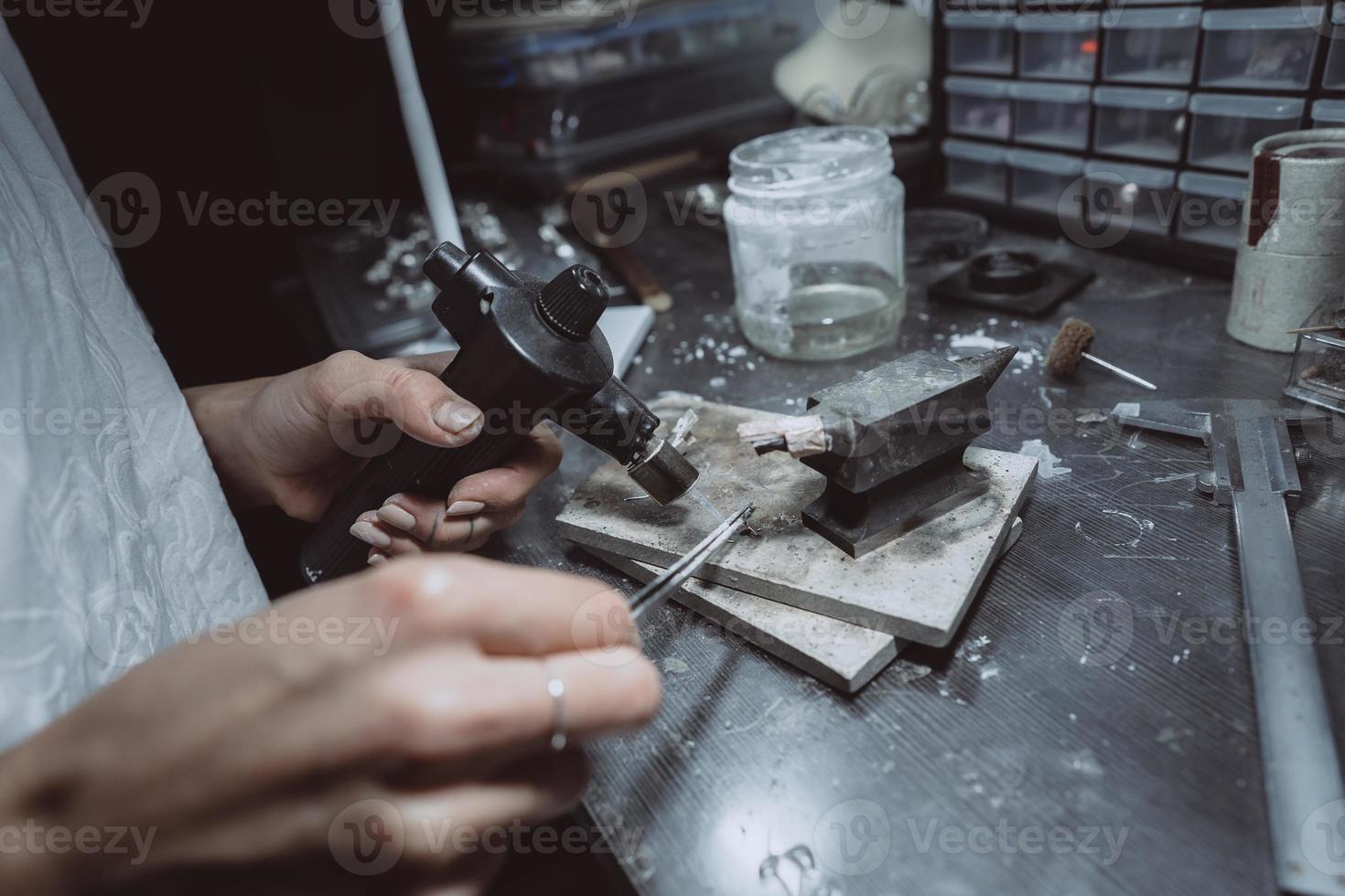 In the workshop, a woman jeweler is busy soldering jewelry photo