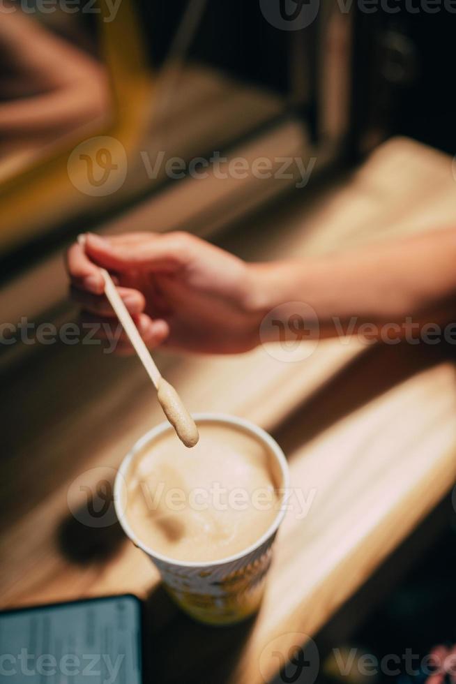 A female hand holding a stick over a latte paper mug photo