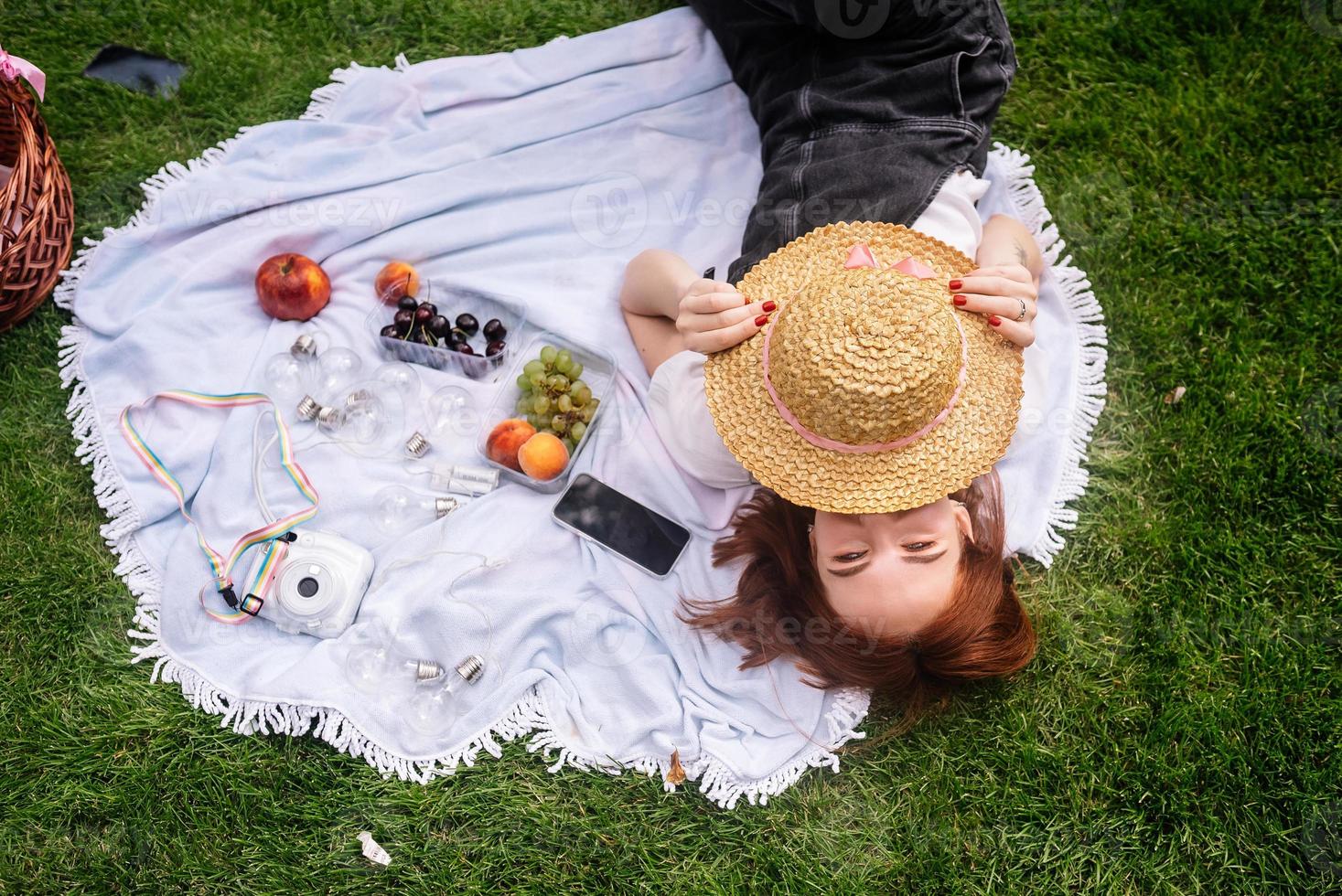 Young woman covers face with a hat while lying on the lawn photo