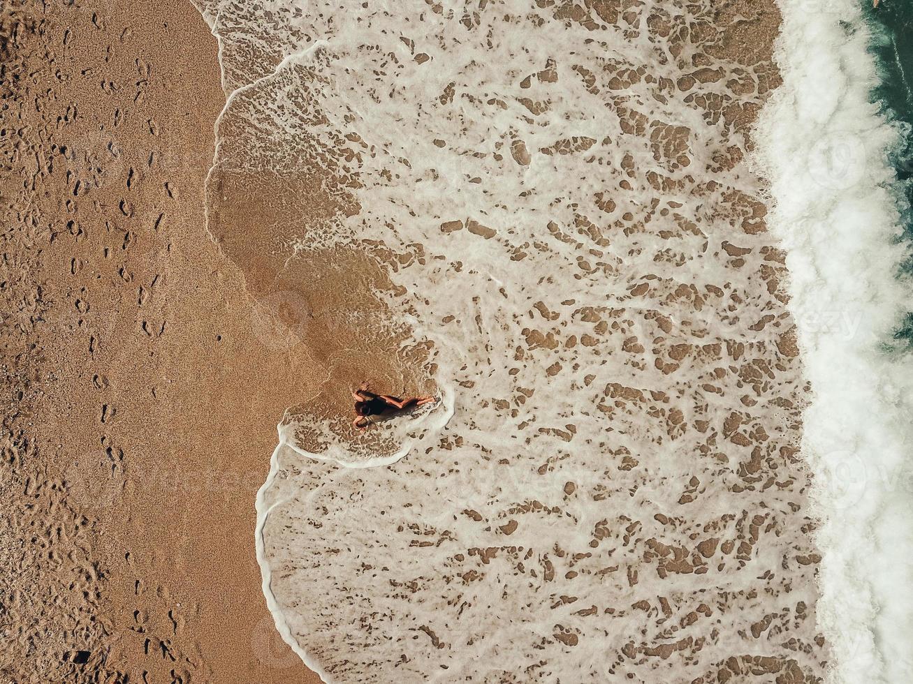 Aerial top view young woman lying on the sand beach and waves photo