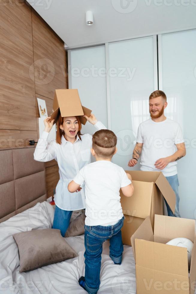papá, mamá y su hijo pequeño juegan en el dormitorio con cajas de papel foto