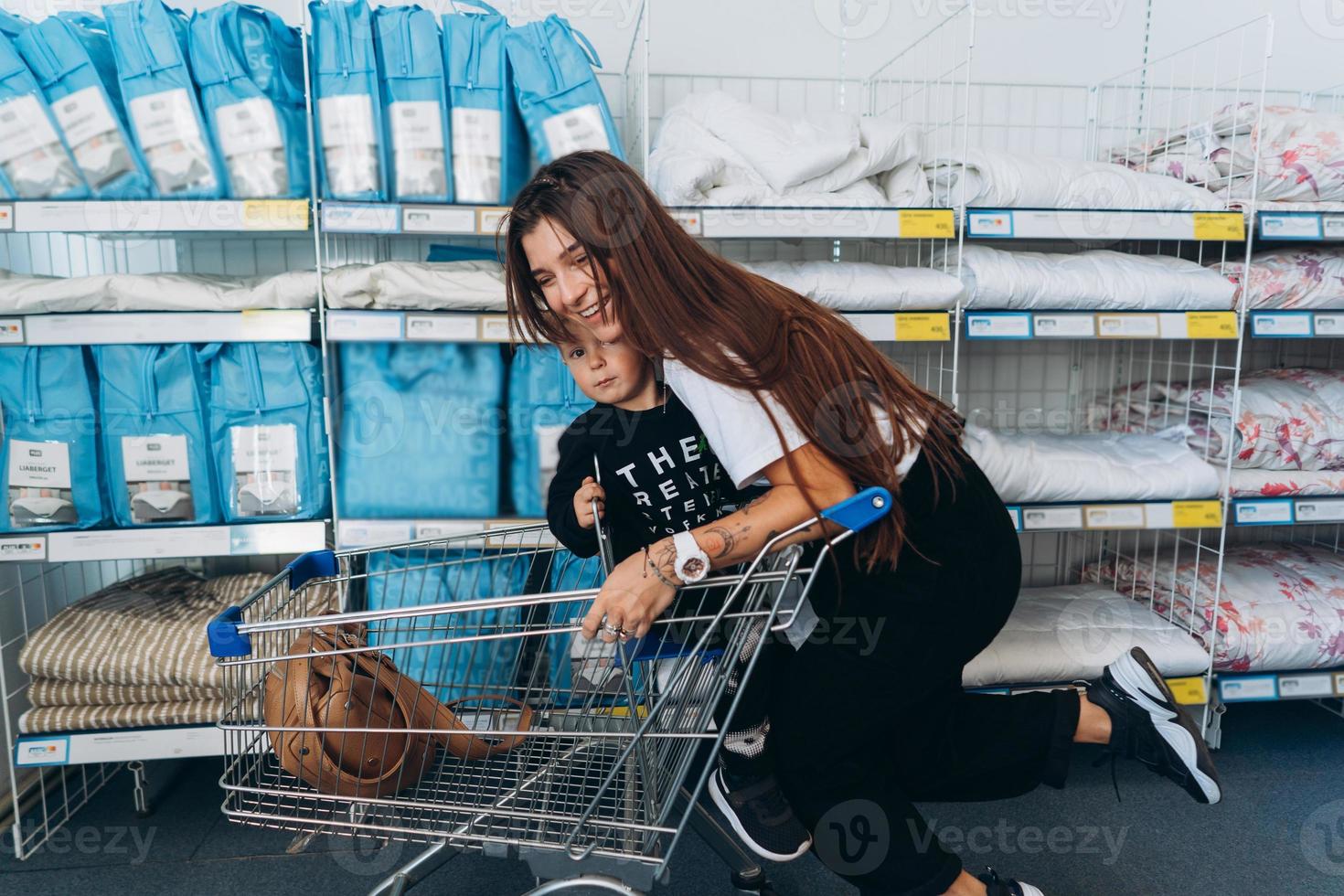 hermosa madre lleva a su pequeño hijo en el carro del supermercado foto