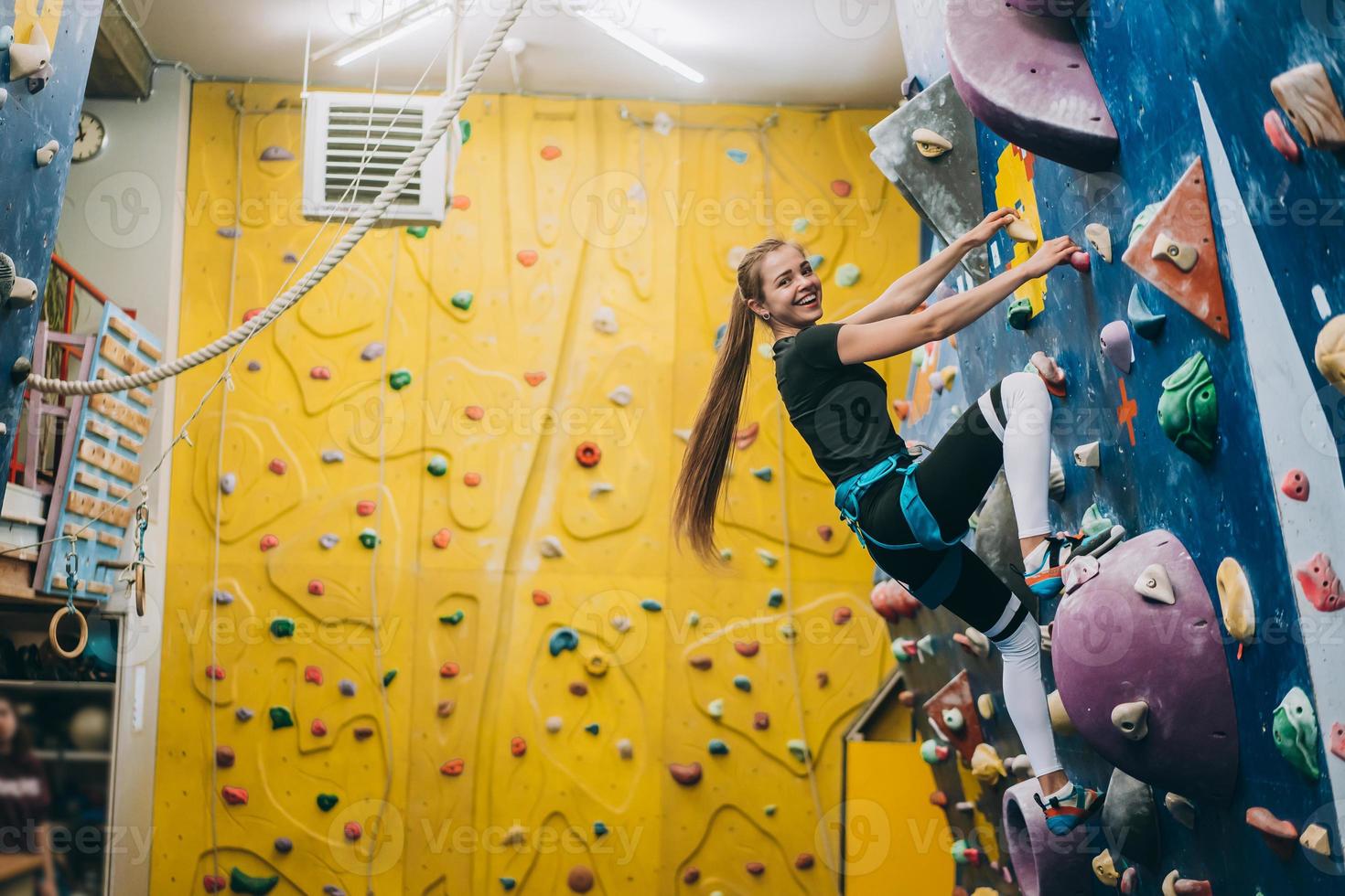 Young woman climbing a tall, indoor, man-made rock climbing wall photo