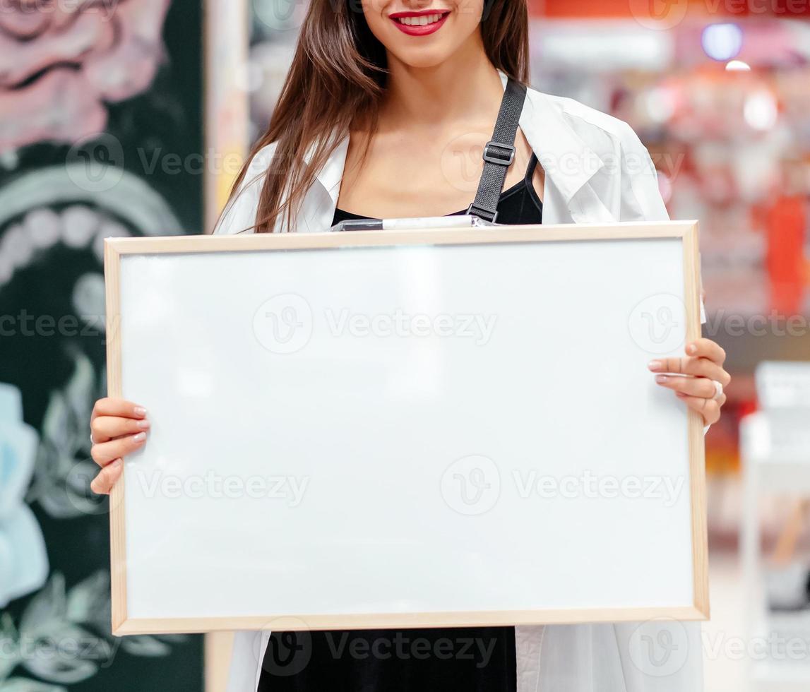 Smiling brunette woman holding white blank board photo