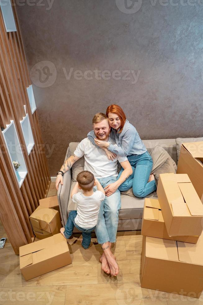 joven familia feliz con niños desempacando cajas juntos sentados en el sofá foto