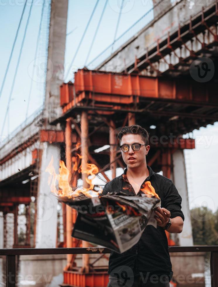 Guy reads a burning newspaper, in the background a bridge photo