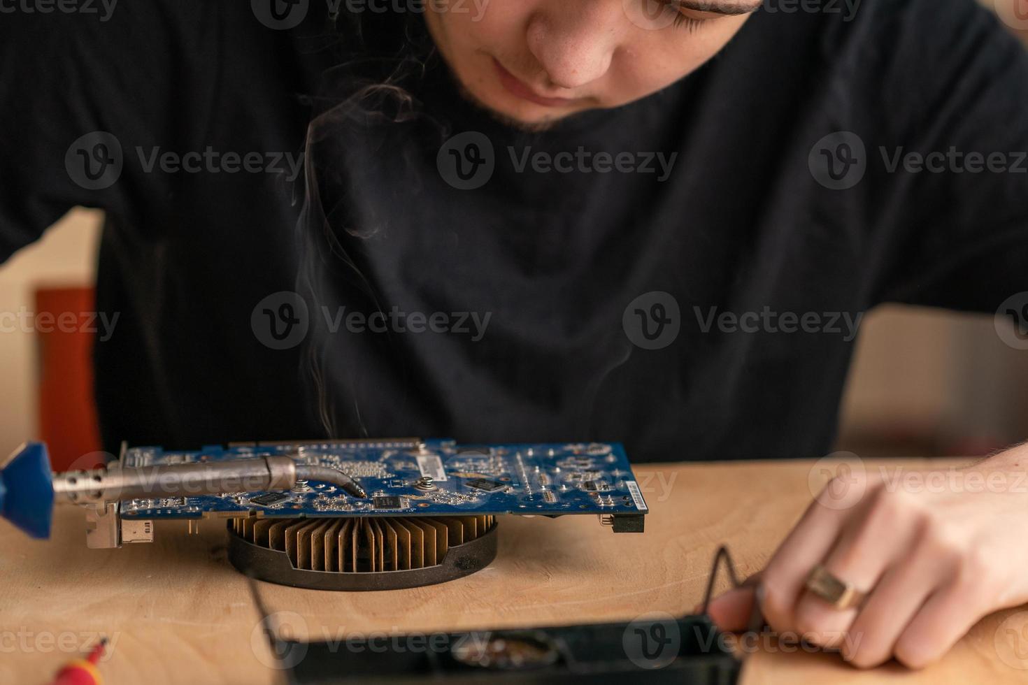 a young man solders a burnt-out microcircuit with a soldering iron photo