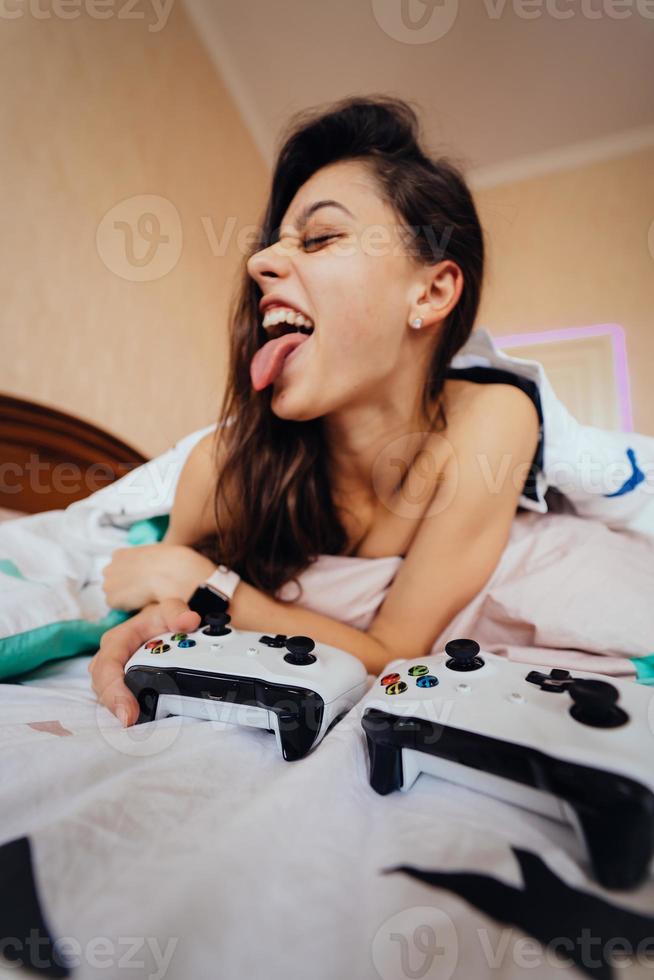 chica divertida acostada en la cama y jugando videojuegos, sosteniendo el controlador foto