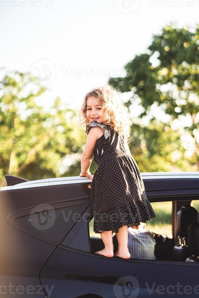 A little girl is standing on the door of the car photo