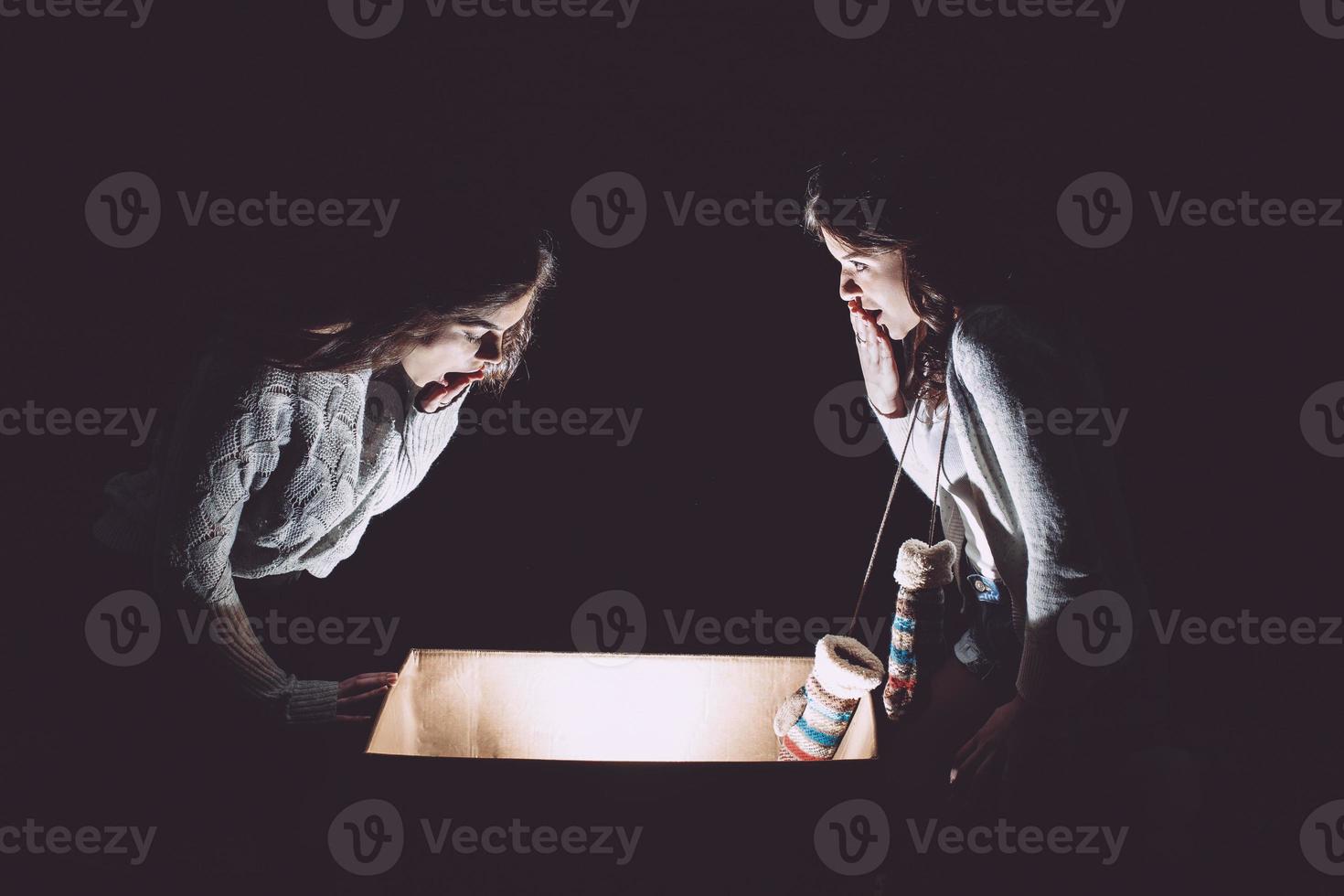 Sisters opens a box with a Christmas present and fascinated looks inside photo