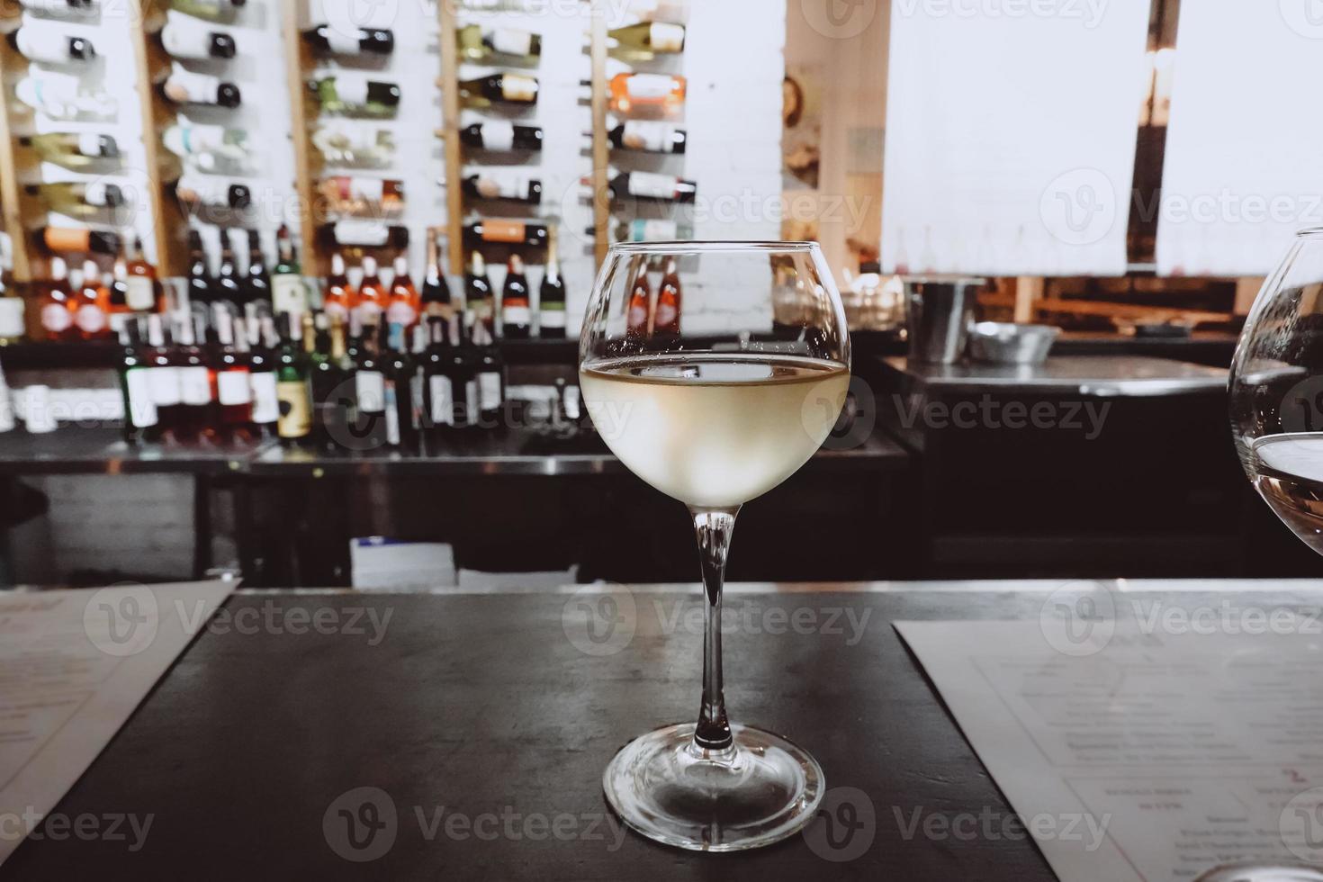 White wine glass on a wooden table, wine bottles collection background photo