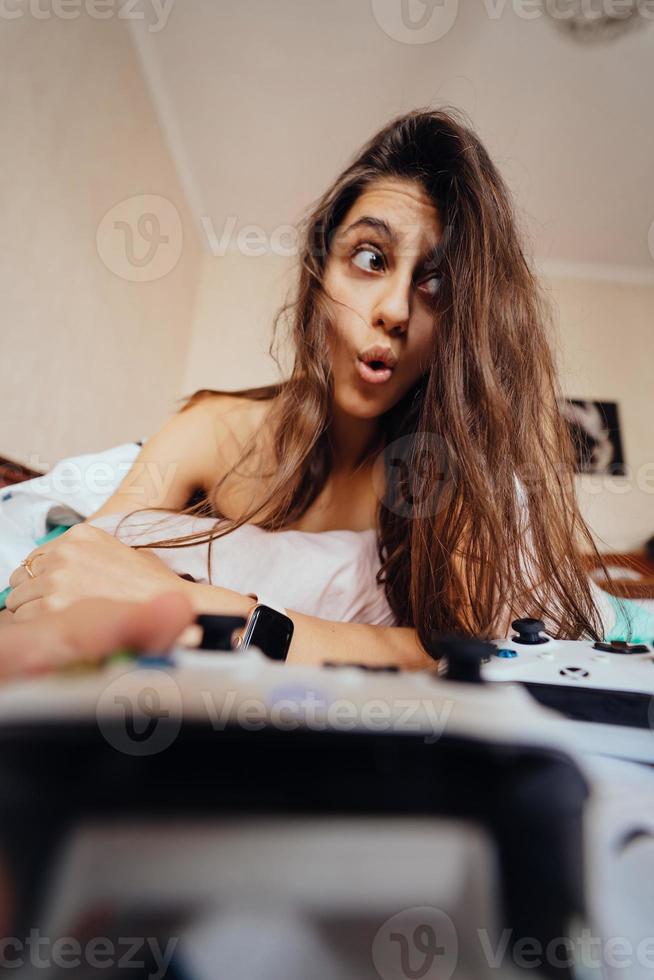 Funny girl lying in bed and playing video game, holding controller photo