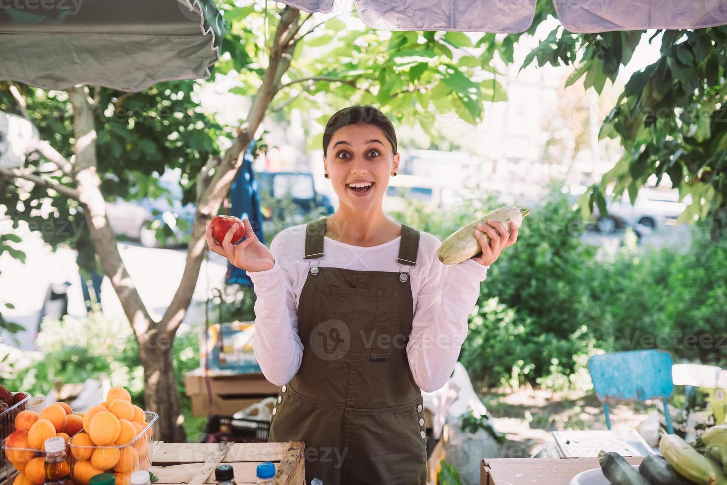 Young saleswoman holding zucchini and tomato in hands photo