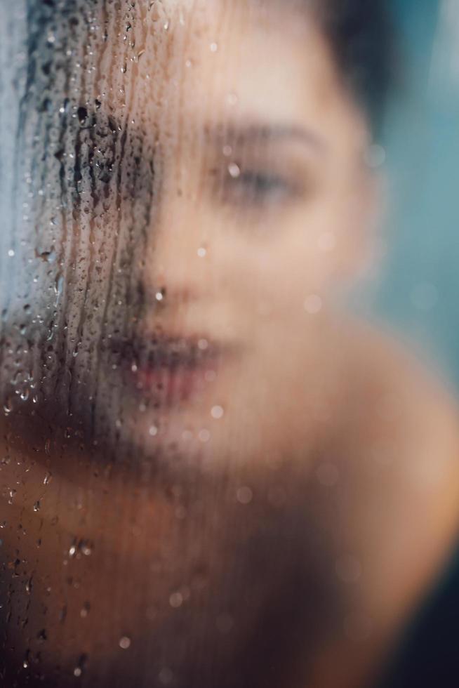 Beautiful woman behind the glass with water drops. photo