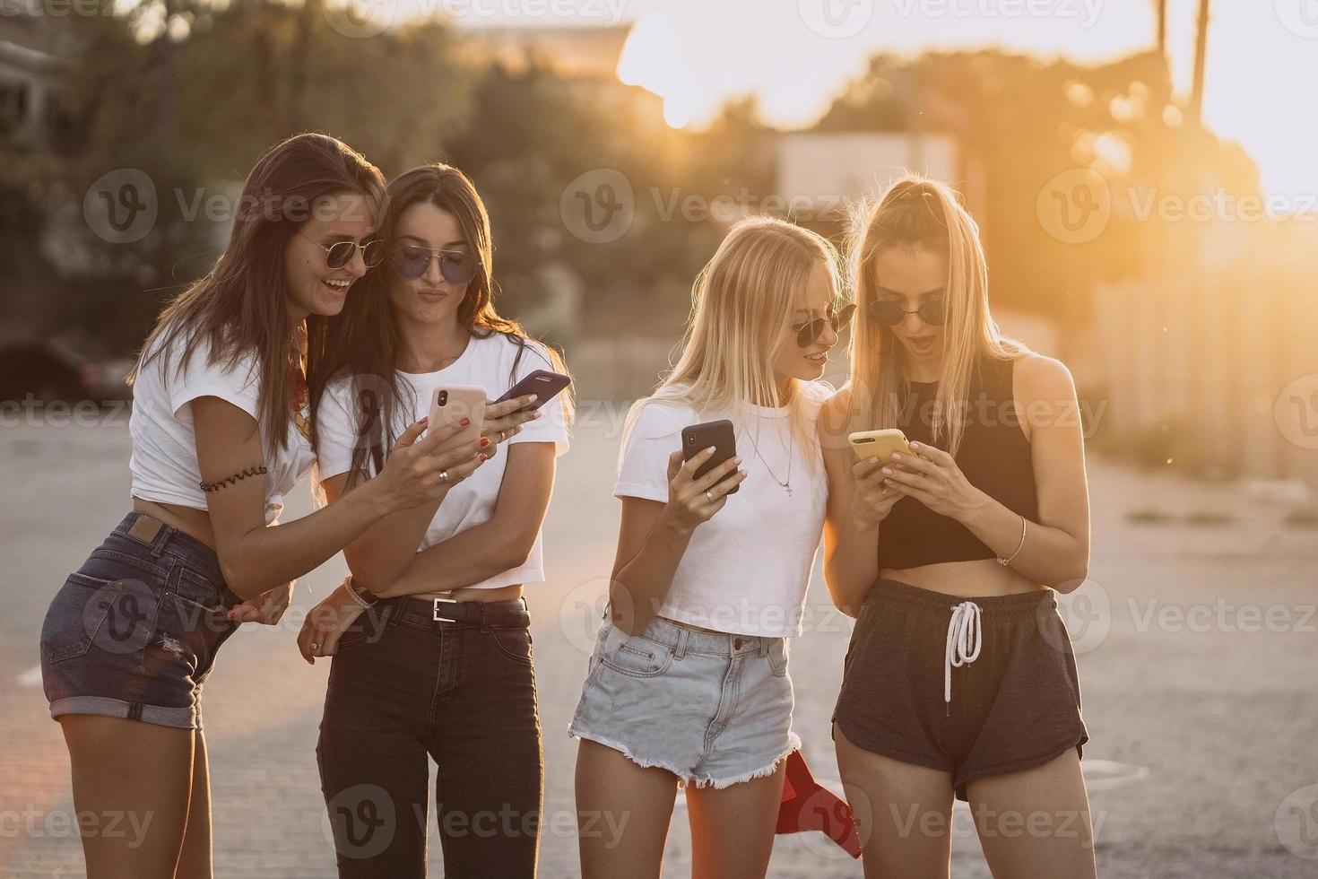 cuatro mujeres atractivas están de pie en el estacionamiento de automóviles con teléfonos inteligentes foto